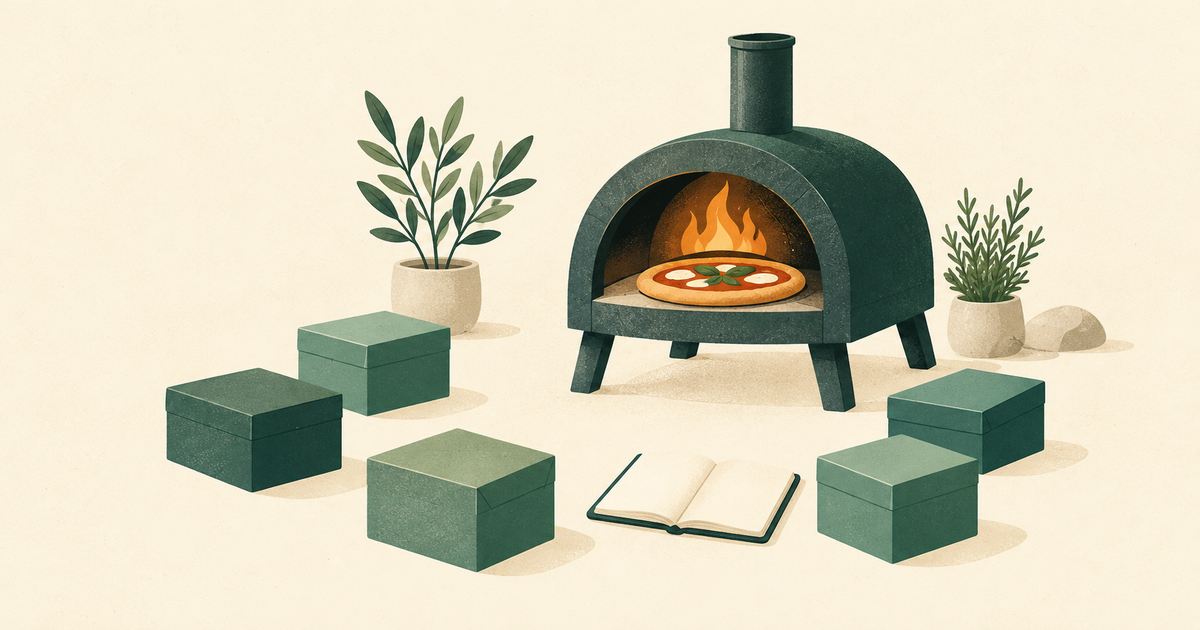 A compact pizza oven sits beside a small controlled ring of boxes and an open notebook.